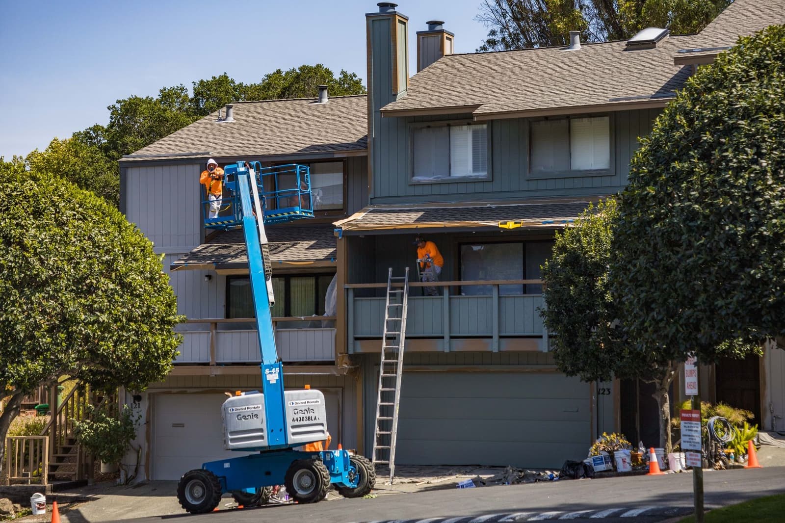 Workers on a boom lift beside a townhouse roof