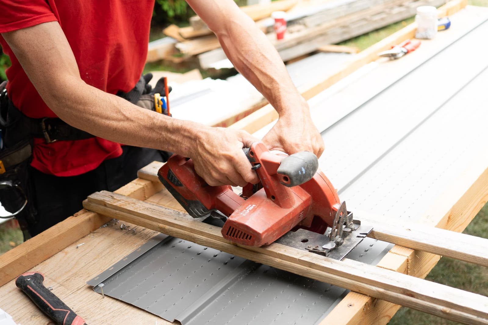 Worker cutting wood beside a metal roof panel