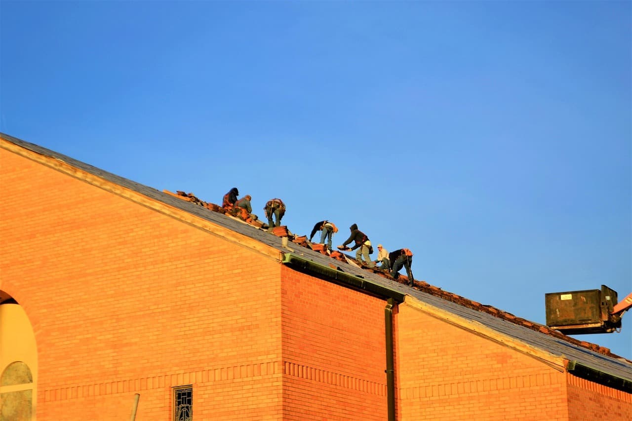 Roofers working on a roof edge of an orange building